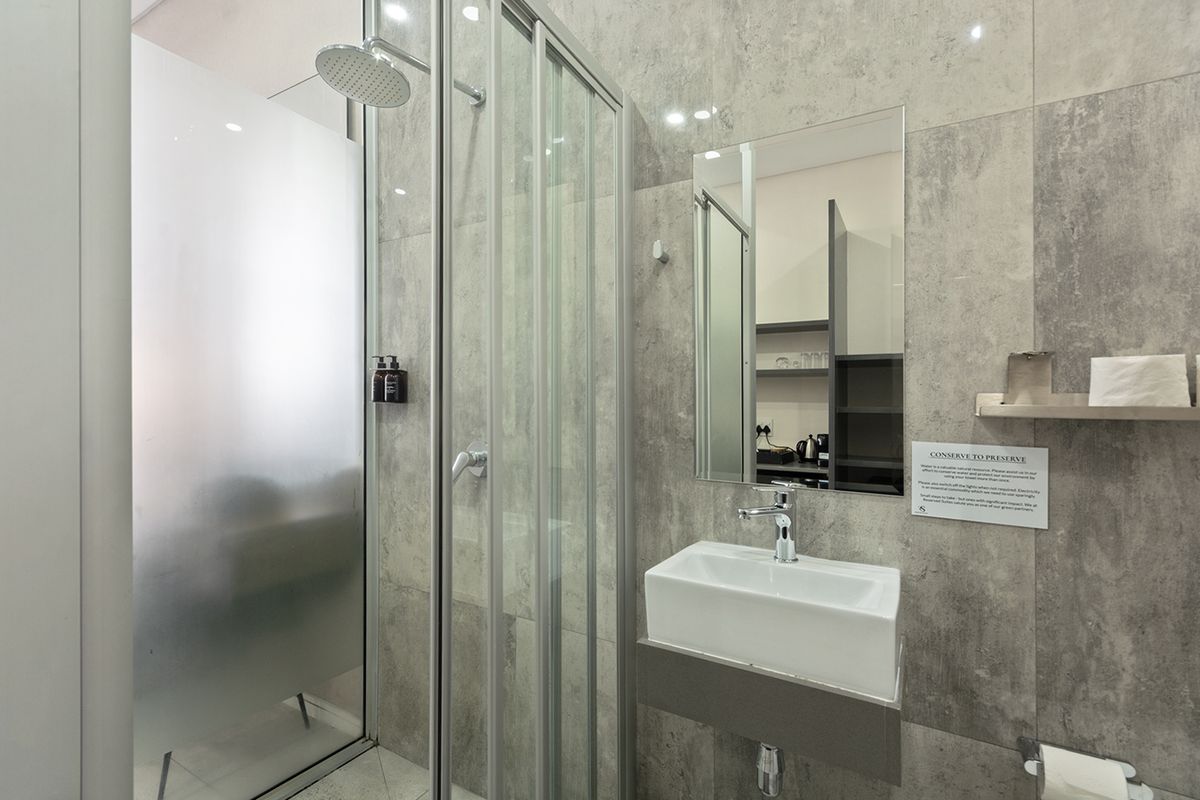 Modern bathroom featuring a glass-enclosed shower with a rain shower head, a wall-mounted basin with chrome fixtures, and contemporary grey wall tiling.