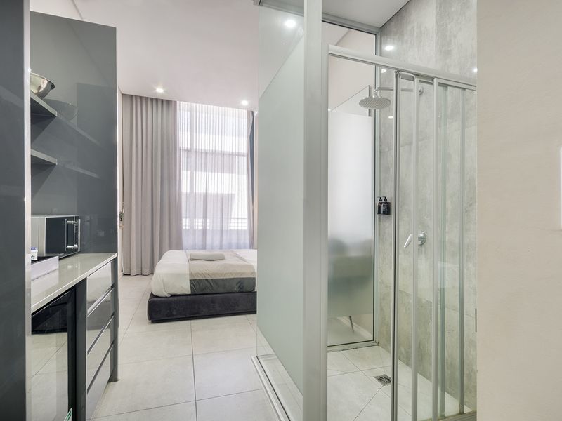 Modern bedroom featuring an integrated glass-enclosed shower, sleek built-in cabinetry, large floor-to-ceiling windows with curtains, and contemporary tiled flooring.