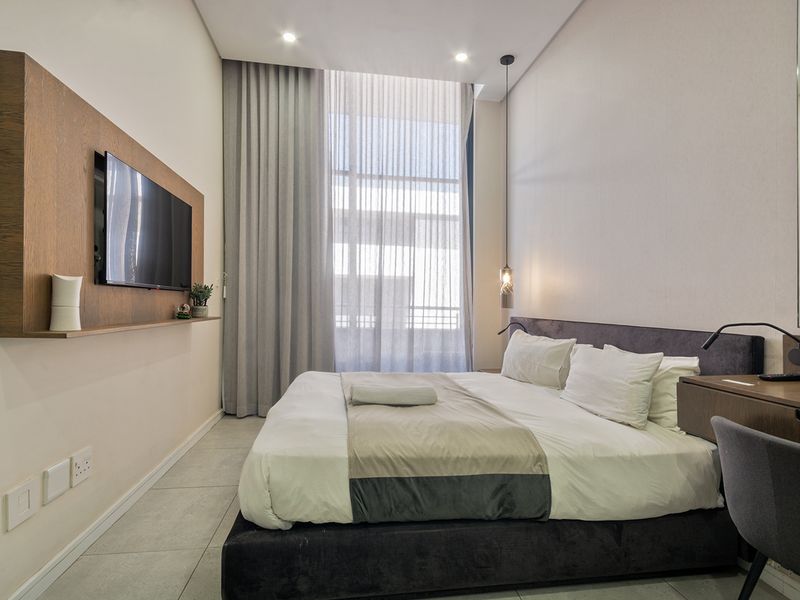 Modern bedroom featuring floor-to-ceiling curtains, tiled flooring, recessed lighting, and a built-in wall-mounted television panel with integrated vanity desk.