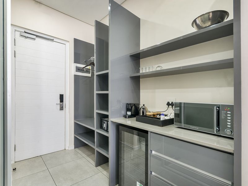 A modern utility space featuring sleek grey built-in cabinetry, stone countertops, integrated shelving, and tiled flooring, providing efficient storage and prep area.