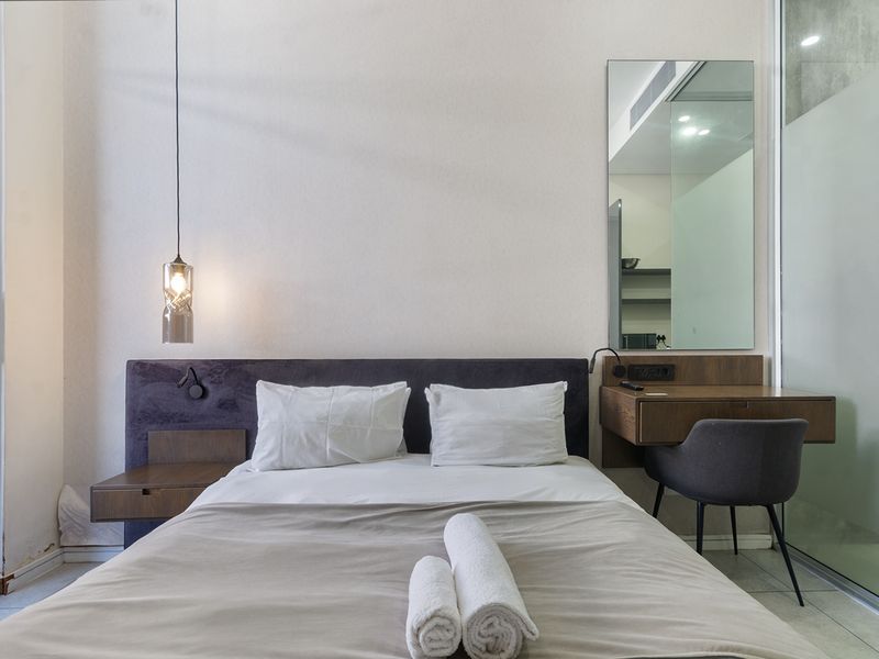Modern bedroom featuring a built-in headboard with integrated floating bedside table, a wall-mounted vanity desk, and tiled flooring with access to a private balcony.