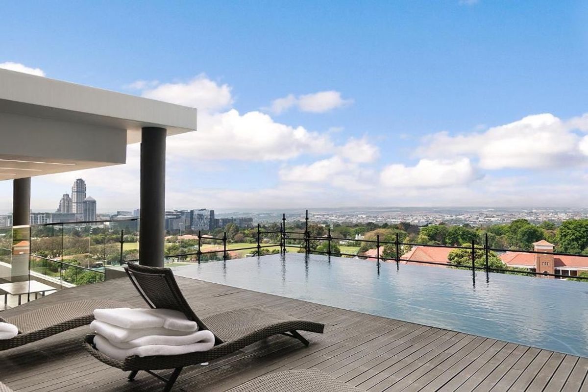 Luxury rooftop infinity pool featuring timber decking, glass balustrades, and expansive panoramic city views.