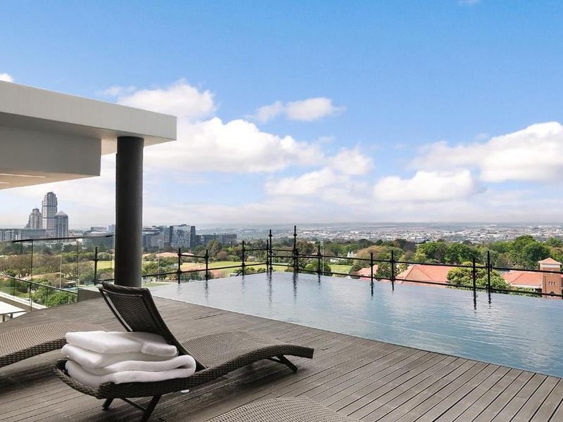 Luxury rooftop infinity pool featuring timber decking, glass balustrades, and expansive panoramic city views.
