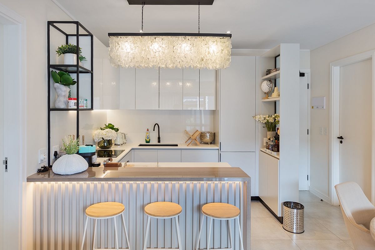 Modern kitchen featuring sleek white cabinetry, stone countertops, integrated appliances, and a stylish breakfast bar with ambient under-counter lighting.