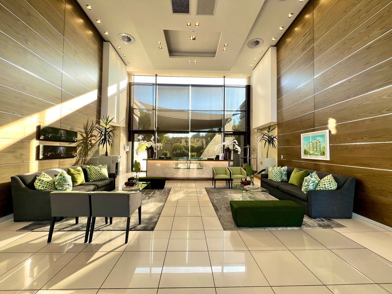A spacious, modern clubhouse lobby featuring high ceilings, wood-paneled walls, polished tile flooring, and a professional reception area with large windows.