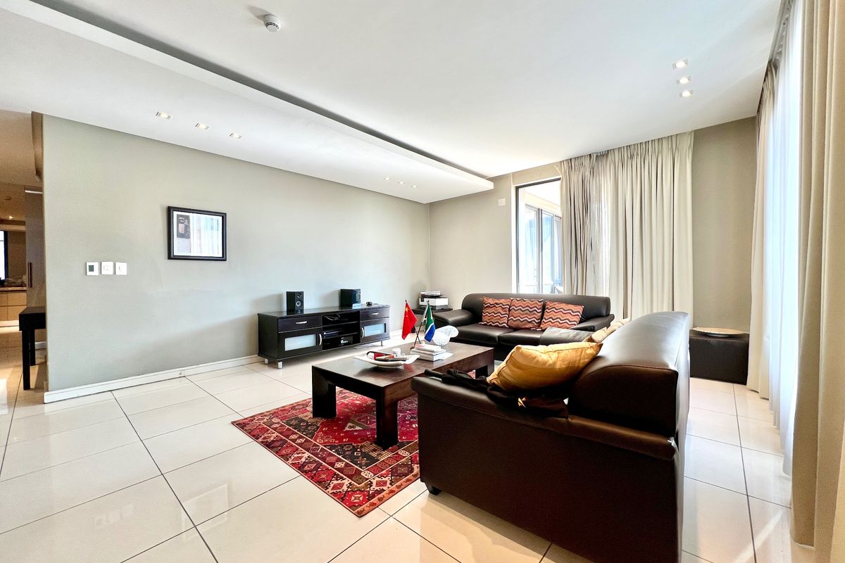 Spacious living room featuring large format floor tiles, recessed ceiling lighting, and floor-to-ceiling curtains leading to an outdoor area.
