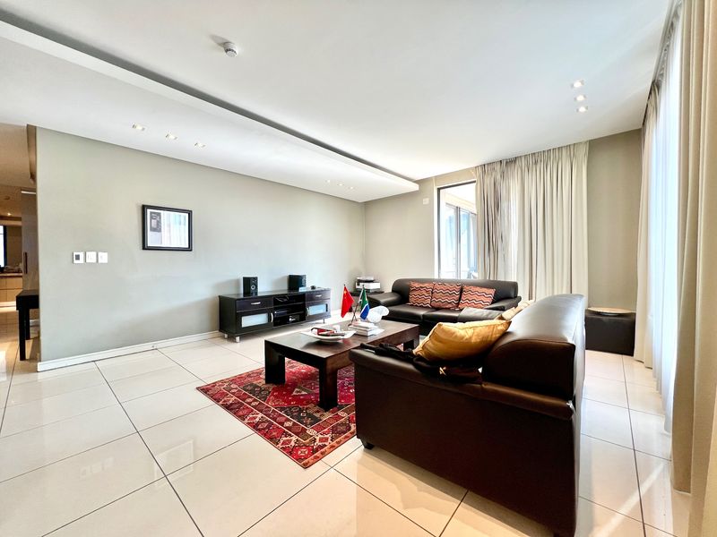 Spacious living room featuring large format floor tiles, recessed ceiling lighting, and floor-to-ceiling curtains leading to an outdoor area.