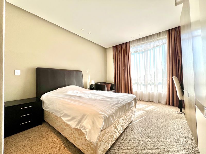 A well-lit bedroom featuring neutral walls, carpet flooring, recessed ceiling lighting, and a large built-in wardrobe with floor-to-ceiling curtains.
