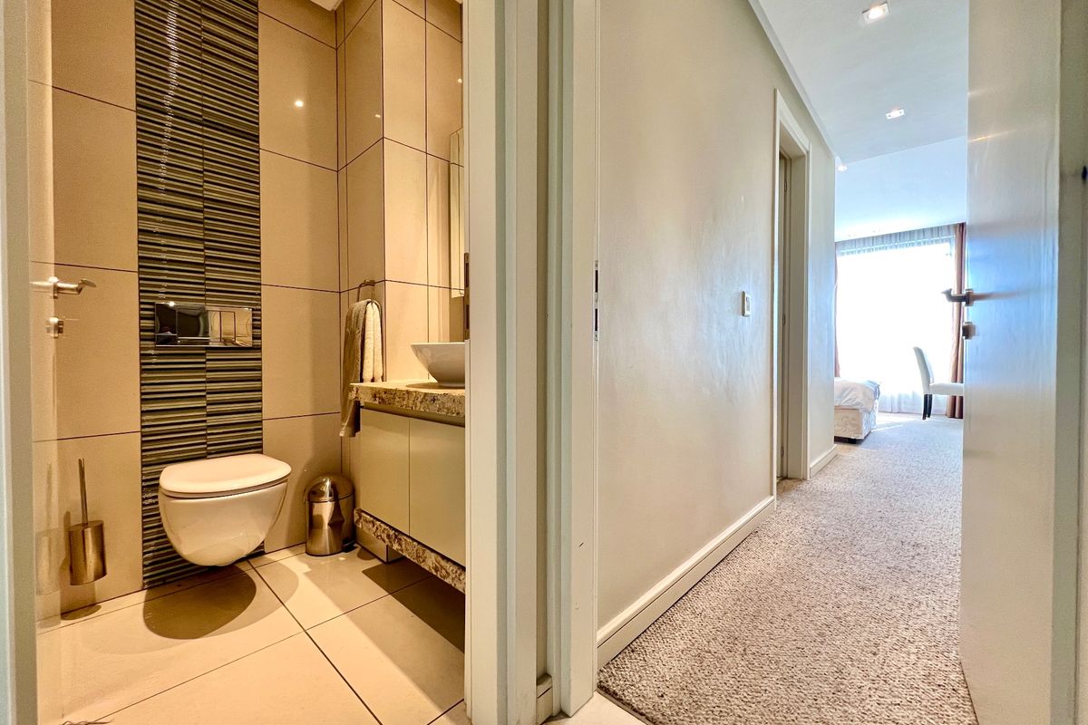 A modern bathroom featuring a wall-hung toilet, vanity with vessel sink, and decorative tiled wall accents, adjacent to a carpeted hallway.