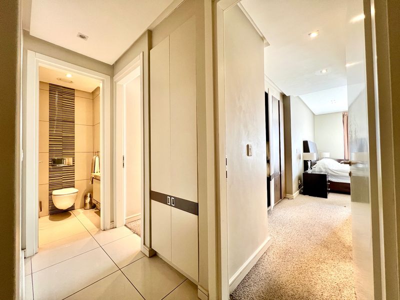 A well-maintained hallway connecting a bedroom and a modern bathroom, featuring built-in storage cupboards and neutral finishes.