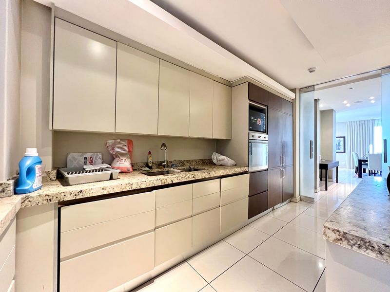 Modern kitchen featuring granite countertops, built-in cabinetry, integrated oven and microwave, and sleek tiled flooring, leading into an adjacent living area.