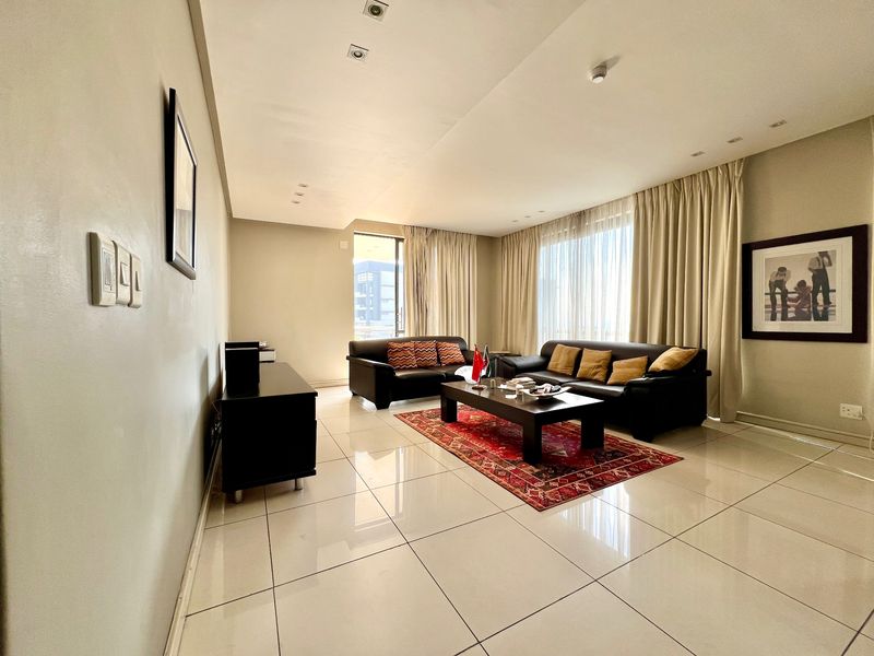 A spacious living room featuring polished tiled flooring, recessed ceiling lighting, and large windows with floor-to-ceiling curtains, creating a bright and comfortable atmosphere.