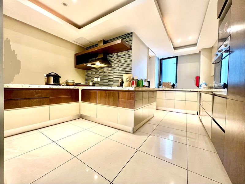 Modern kitchen featuring two-tone cabinetry, stone countertops, mosaic backsplash, built-in oven, and recessed ceiling lighting with tiled flooring.