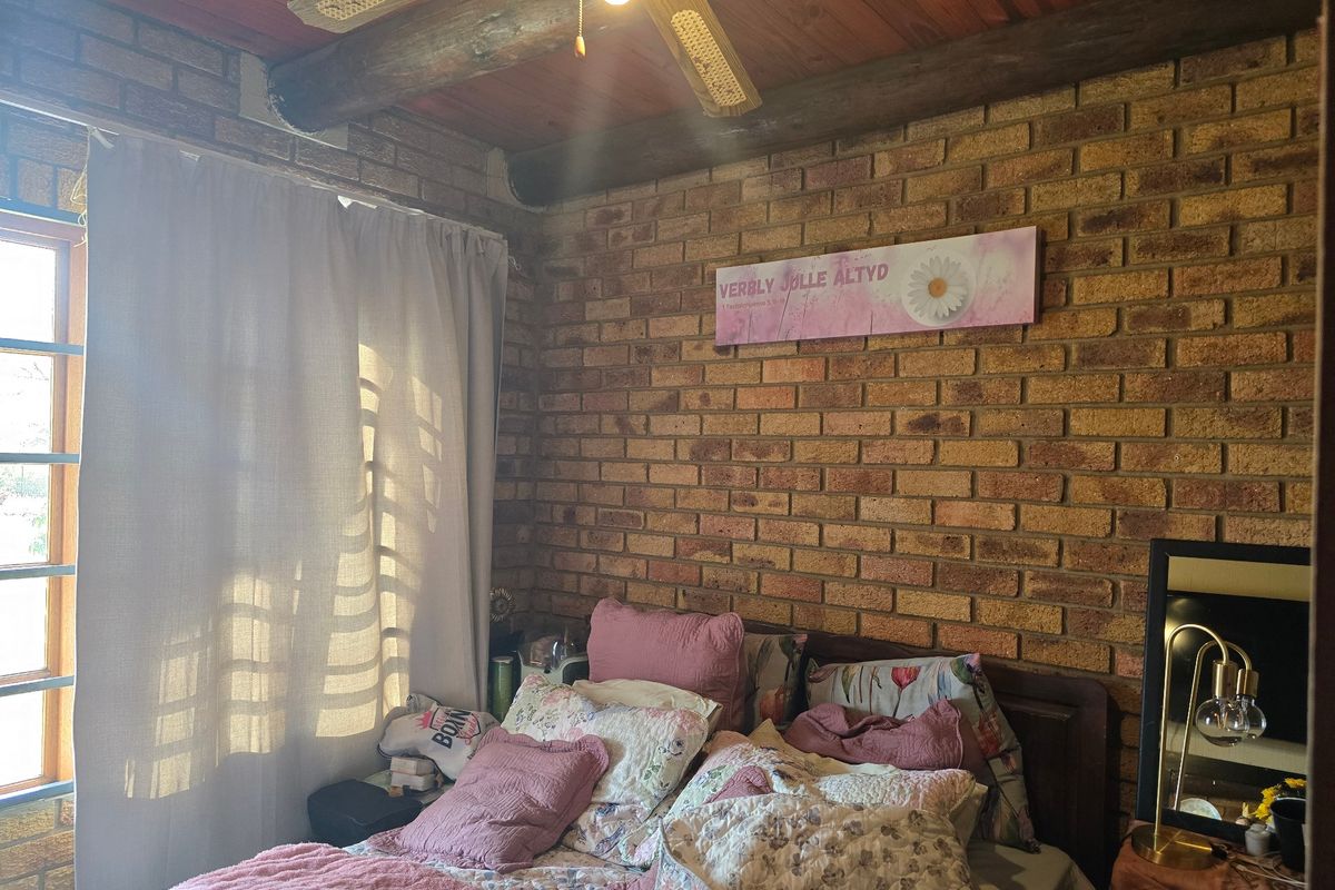 A cozy bedroom featuring rustic exposed brick walls and a timber ceiling with an integrated ceiling fan.
