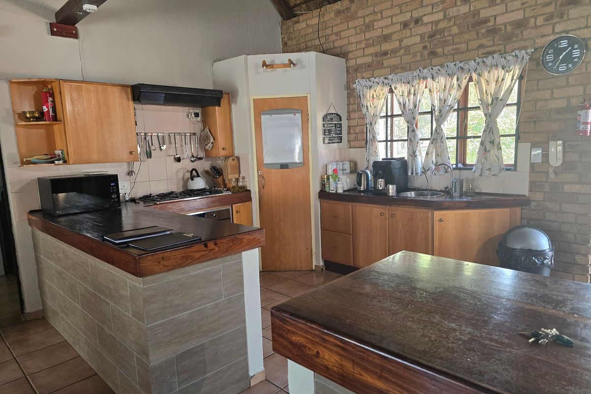 A rustic kitchen featuring wooden cabinetry, exposed brick walls, a thatched ceiling, and a central island with a dark timber countertop.