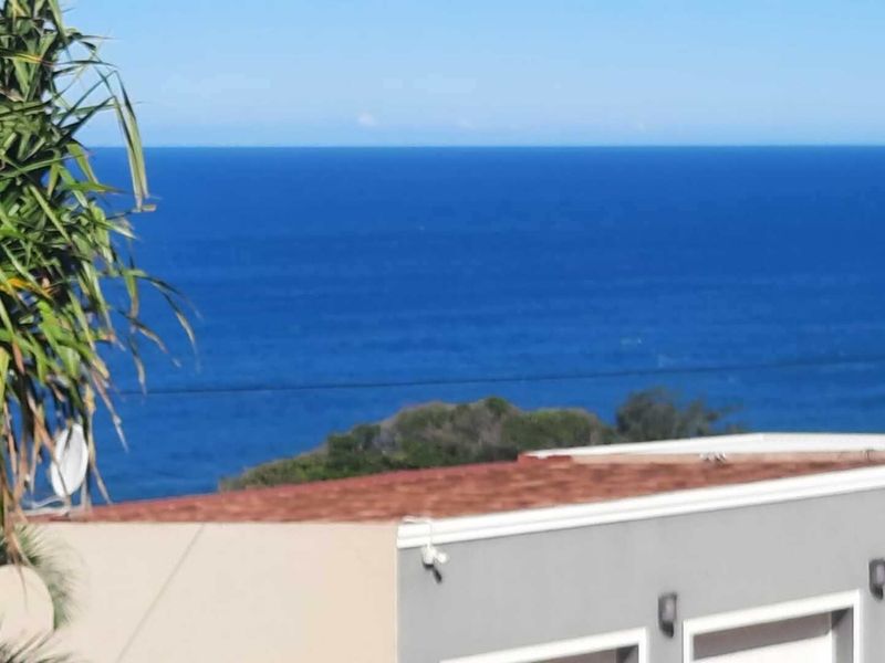 A scenic elevated view overlooking the ocean, featuring a clear horizon line and the roofline of the property.