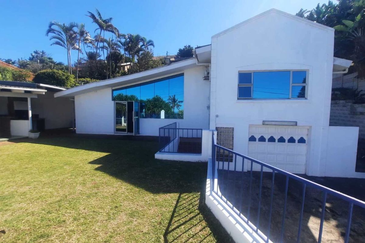 Rear view of the property featuring a lawn, covered patio area, and a single garage with reflective windows.