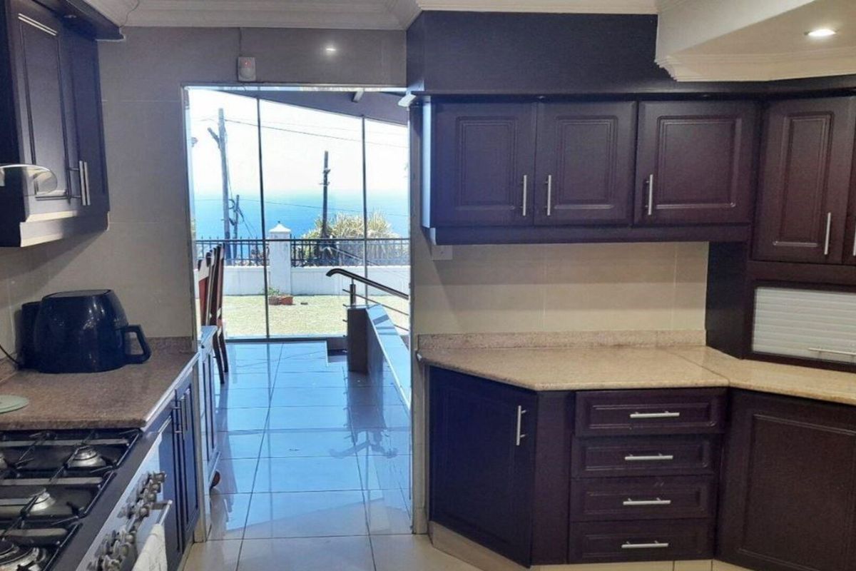 A functional kitchen featuring dark wood cabinetry, granite countertops, and a gas hob, with direct access to an outdoor patio area.