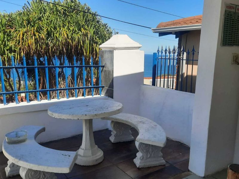 An outdoor patio area featuring tiled flooring, masonry pillars, and metal security fencing, offering a view of the ocean.