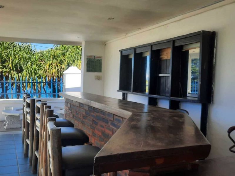An outdoor covered bar area featuring a brick-based counter, wall-mounted shelving, and tiled flooring, offering a functional space for entertainment.