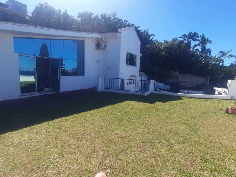 Rear view of the property featuring a spacious lawn, large glass sliding doors, and a secure boundary wall with metal balustrades.