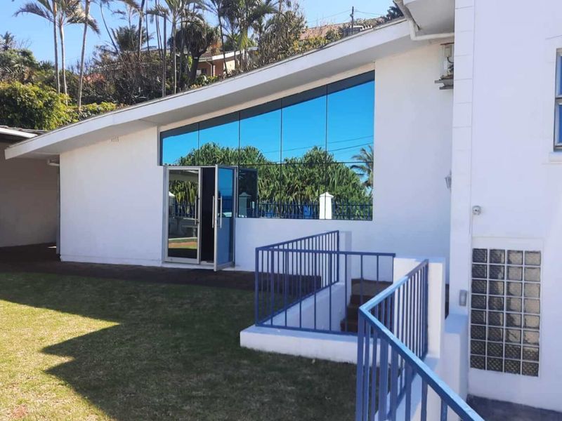 Rear exterior view of the property featuring a modern glass facade, metal railings, and a paved patio area adjacent to the lawn.