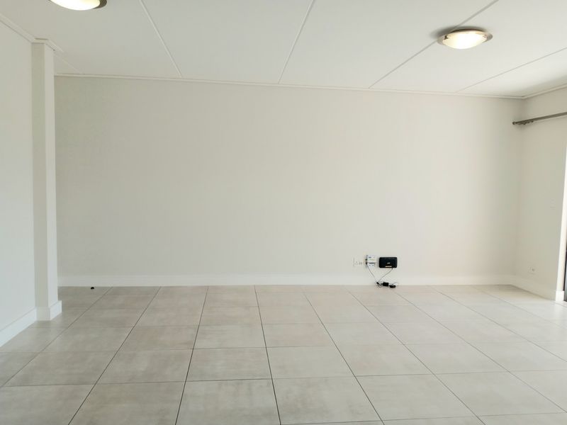 A bright, empty living area featuring neutral tiled flooring, clean white walls, and modern recessed ceiling lighting.