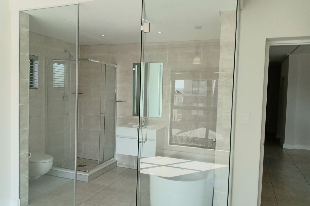 Modern bathroom featuring a glass-enclosed shower, wall-mounted vanity, and wall-hung toilet with neutral floor-to-ceiling tiling and contemporary finishes.
