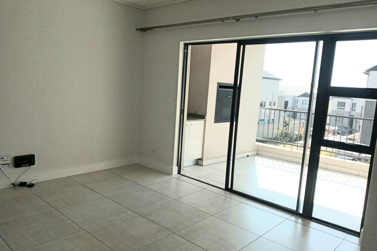 An empty, well-maintained living area featuring neutral tiled flooring and large sliding glass doors that provide access to an outdoor balcony.