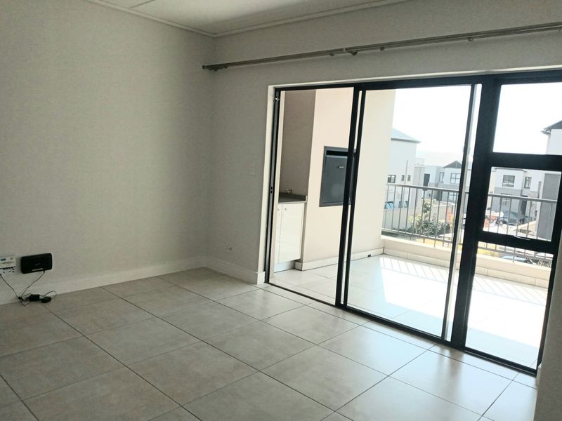 An empty, well-maintained living area featuring neutral tiled flooring and large sliding glass doors that provide access to an outdoor balcony.