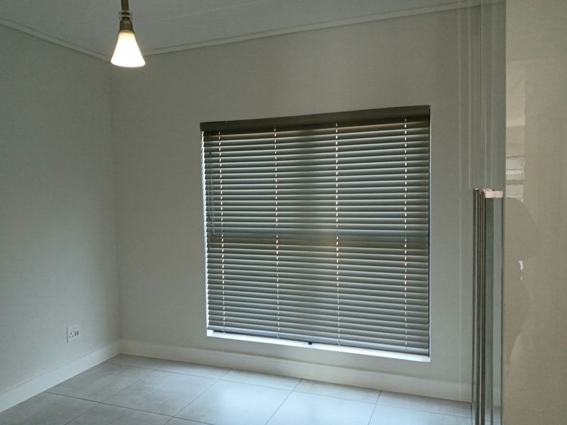 A clean, empty bedroom featuring neutral tiled flooring, white walls, and fitted venetian blinds, providing a blank canvas for personalization.
