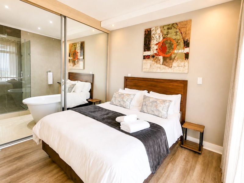 Modern bedroom featuring laminate flooring, recessed lighting, and mirrored sliding wardrobe doors with direct access to an en-suite bathroom.