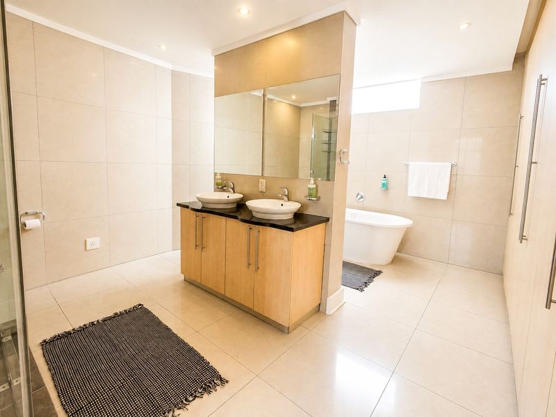 Modern bathroom featuring a double vanity with vessel sinks, a freestanding bathtub, and neutral floor-to-ceiling tiling.
