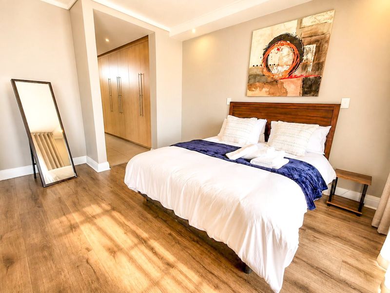 A well-maintained bedroom featuring warm laminate flooring, recessed downlighting, and ample built-in cupboard space in the adjacent dressing area.