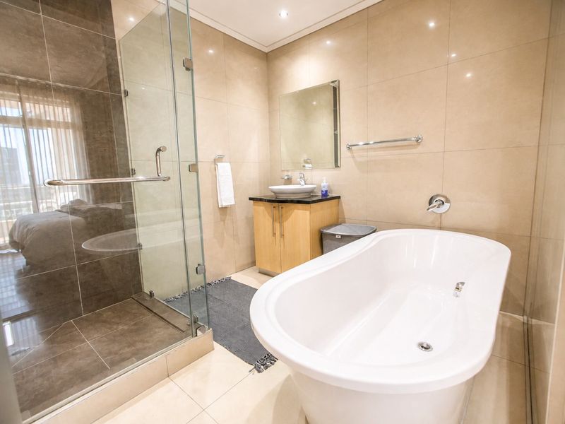 Modern bathroom featuring a freestanding bathtub, a separate glass-enclosed shower, and a vanity with a vessel sink, finished with neutral wall and floor tiles.