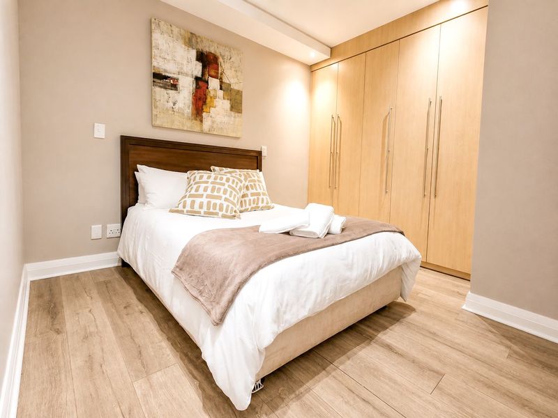 A well-maintained bedroom featuring light wood-tone laminate flooring and extensive floor-to-ceiling built-in cabinetry with modern hardware.