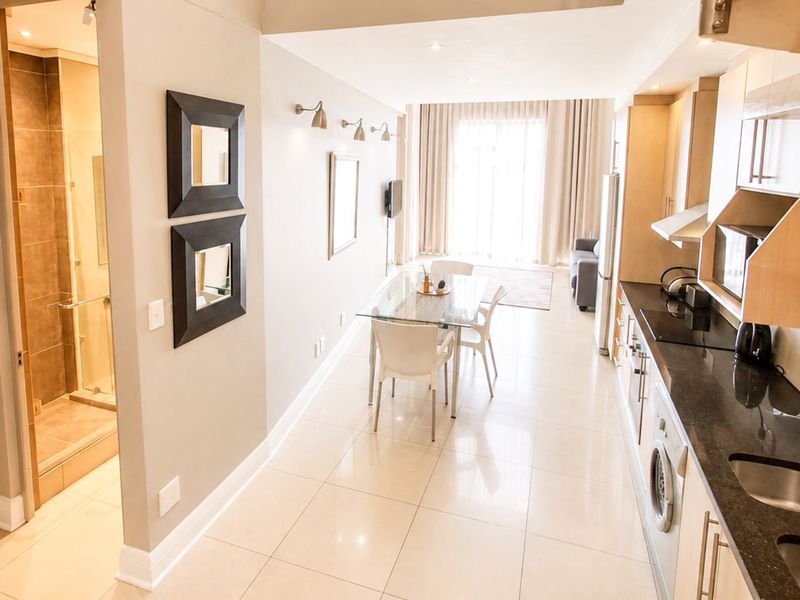Modern open-plan apartment featuring a sleek kitchen with granite countertops, integrated appliances, and tiled flooring, seamlessly flowing into the dining and living area.