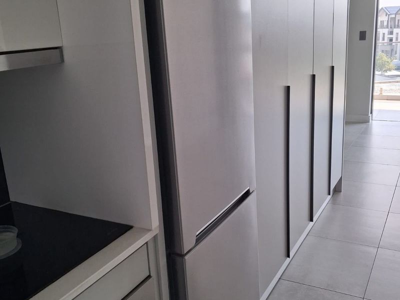 Modern kitchen featuring sleek grey cabinetry, integrated refrigerator, built-in oven, and electric cooktop with neutral tiled flooring.