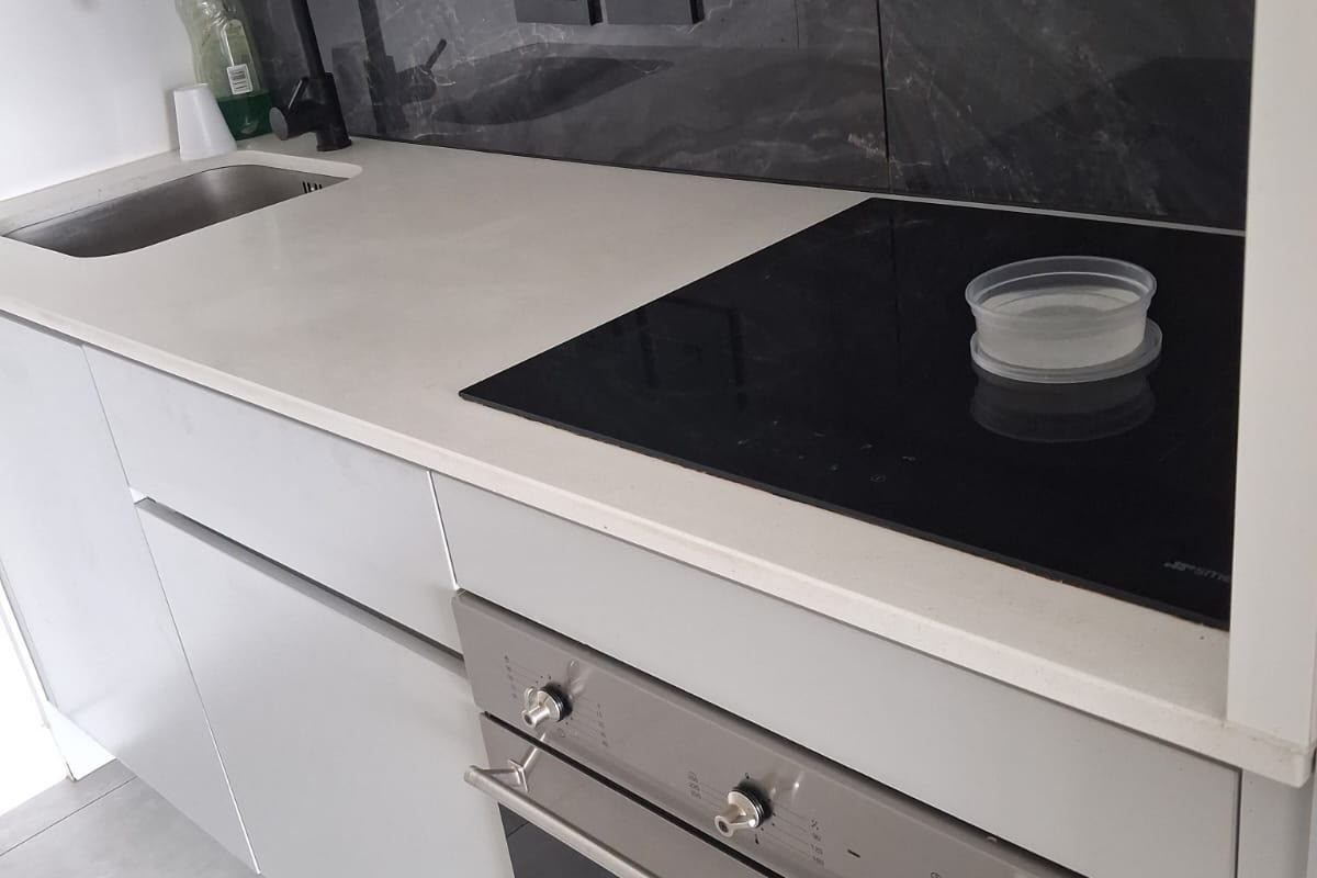 Modern kitchen area featuring a sleek stone countertop, integrated electric hob, built-in oven, and a stylish dark marble-look splashback with a contemporary mixer tap.