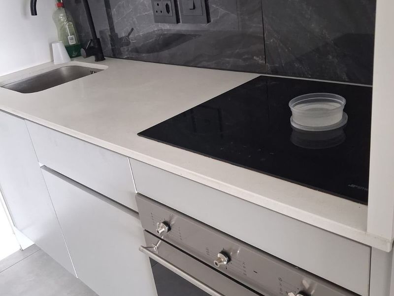 Modern kitchen area featuring a sleek stone countertop, integrated electric hob, built-in oven, and a stylish dark marble-look splashback with a contemporary mixer tap.