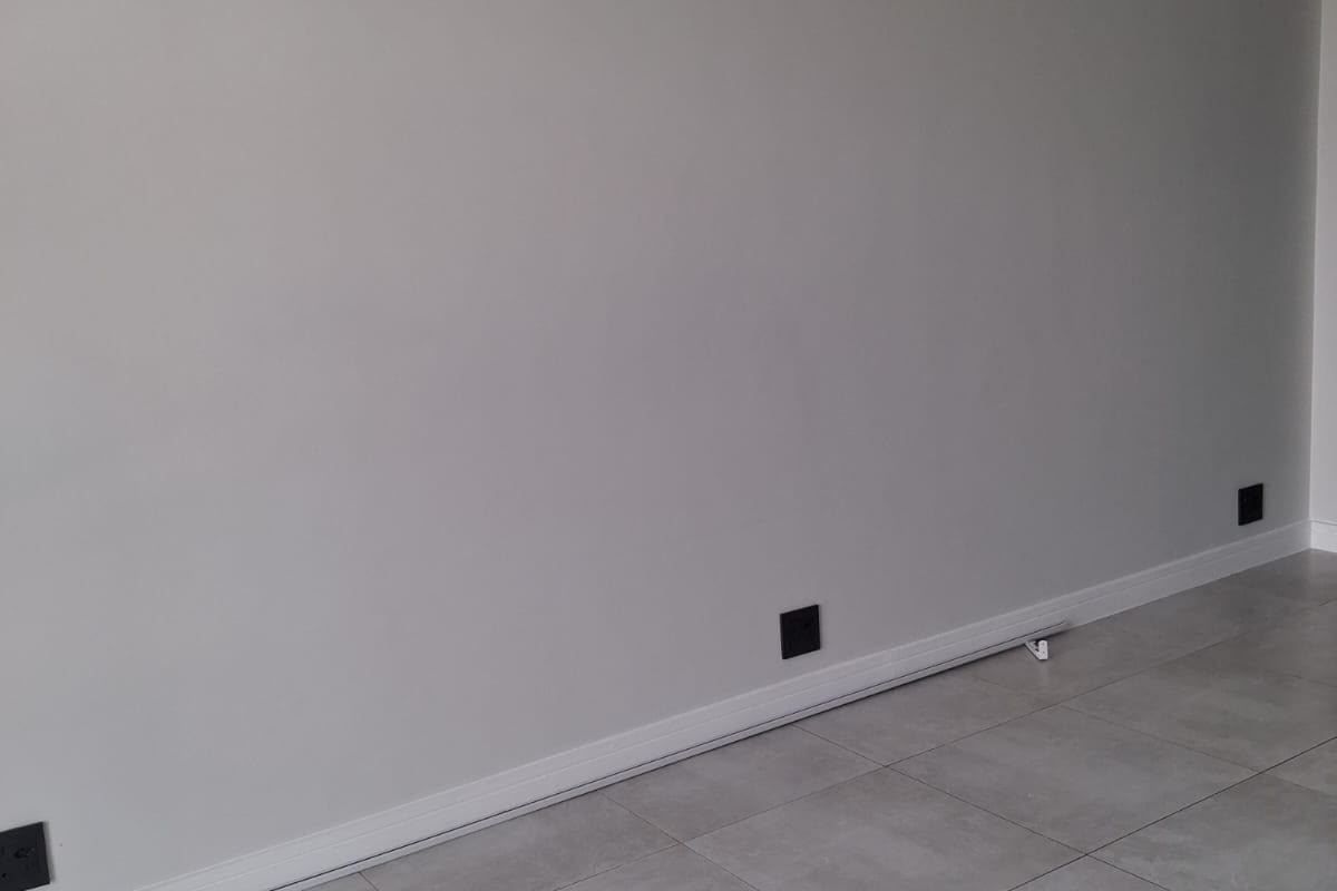 A clean, empty living space featuring modern grey porcelain tile flooring, neutral walls, and contemporary black electrical fixtures.