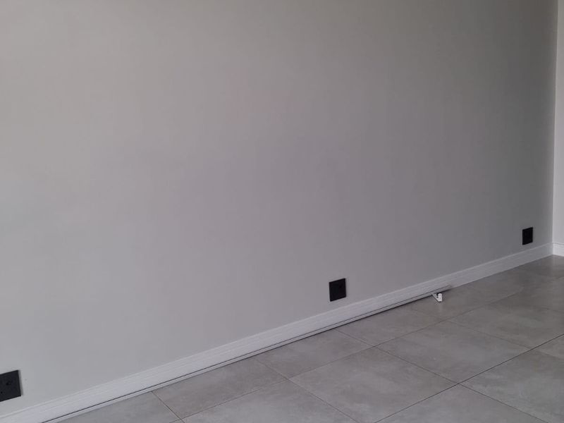 A clean, empty living space featuring modern grey porcelain tile flooring, neutral walls, and contemporary black electrical fixtures.