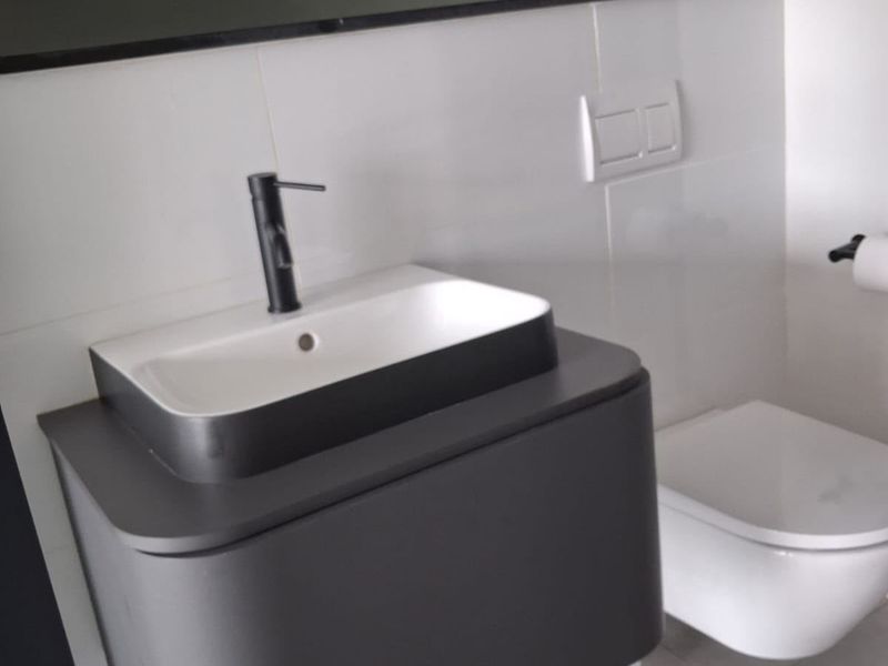 Modern bathroom featuring a wall-mounted vanity with a vessel sink, black faucet, and a wall-hung toilet with a sleek flush plate.
