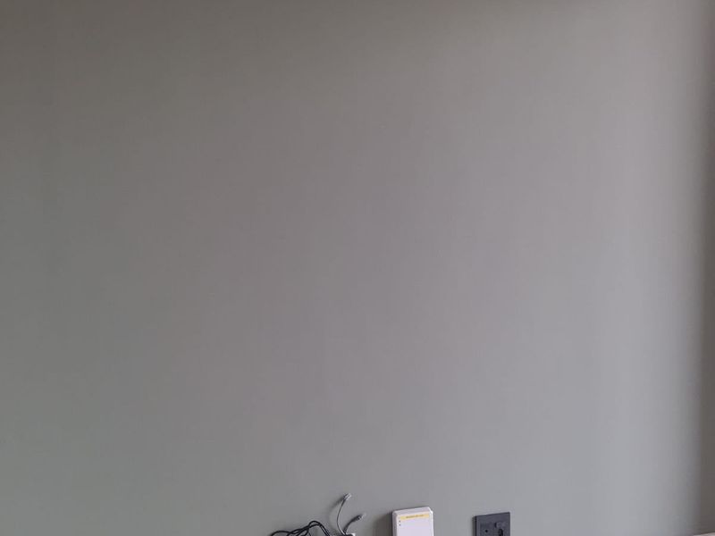 A plain interior wall featuring grey paint, tiled flooring, skirting boards, and installed electrical and data connectivity points.