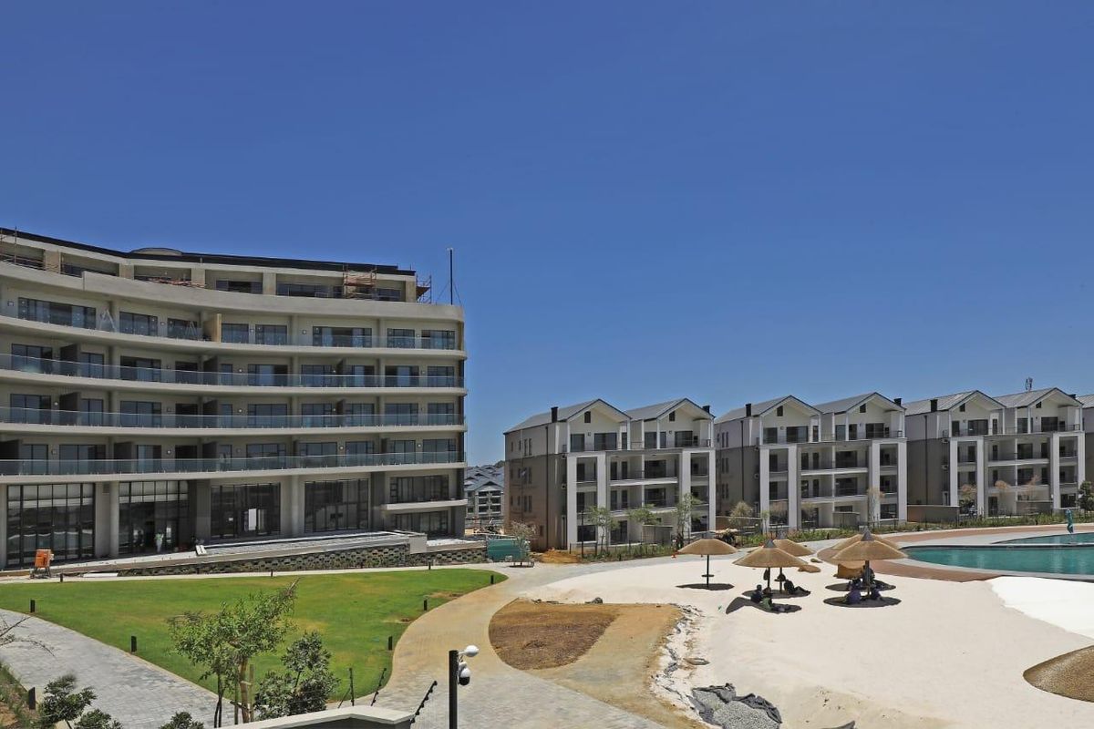 A view of a modern apartment complex featuring landscaped gardens, paved walkways, and a swimming pool area with communal facilities.