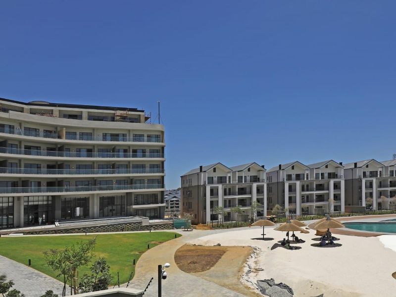 A view of a modern apartment complex featuring landscaped gardens, paved walkways, and a swimming pool area with communal facilities.