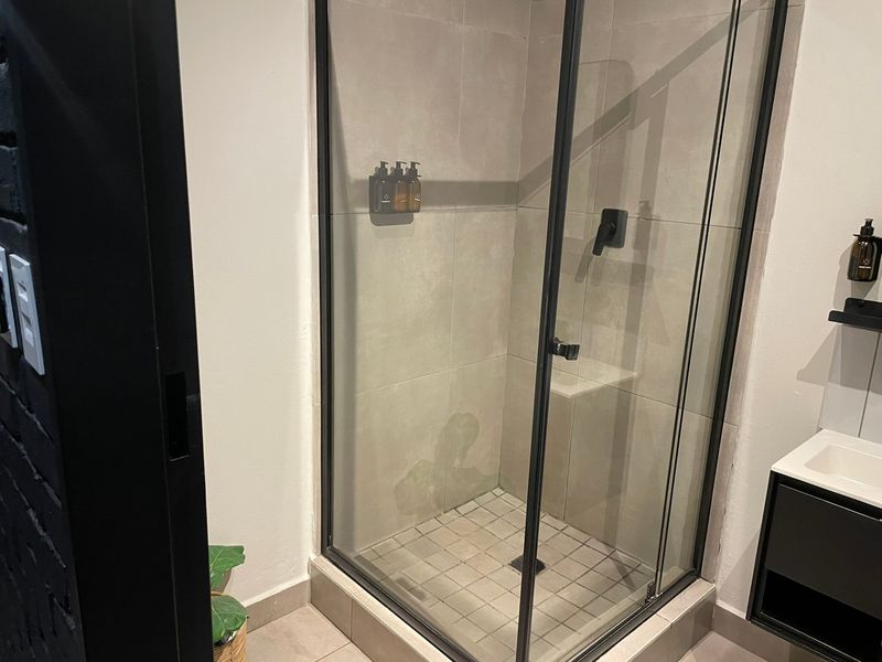 Modern bathroom featuring a glass-enclosed shower with a built-in bench, black fixtures, and a sleek vanity cabinet.
