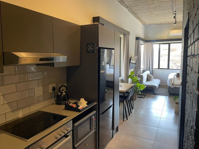Modern open-plan apartment featuring a sleek kitchen with built-in appliances, subway tile backsplash, exposed concrete ceilings, and tiled flooring throughout.