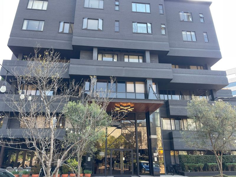Modern apartment building exterior featuring a dark brick facade, large glass windows, and a prominent entrance canopy with integrated lighting.