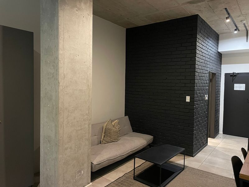 Modern living area featuring an exposed concrete ceiling, a striking black painted brick feature wall, and industrial-style concrete column detailing.